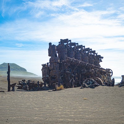 千鳥ヶ浜の沈船のエンジンなどの残骸と強い風で流れるしぶきに霞む砂浜の奥に立つ摺鉢山の写真