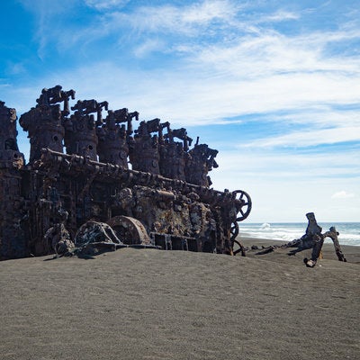 青空と海を背に砂浜に聳え立つ沈船のエンジンの写真
