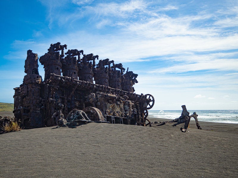 Shipwreck Engine Towering on Sandy Beach Against Blue Sky and Sea