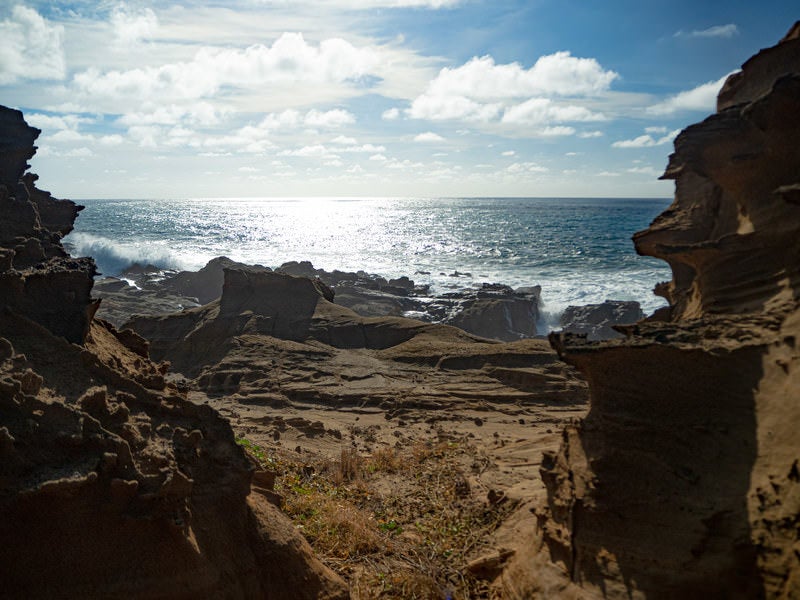 激しく寄せる波の飛沫でかすむ釜岩の波打ち際の写真