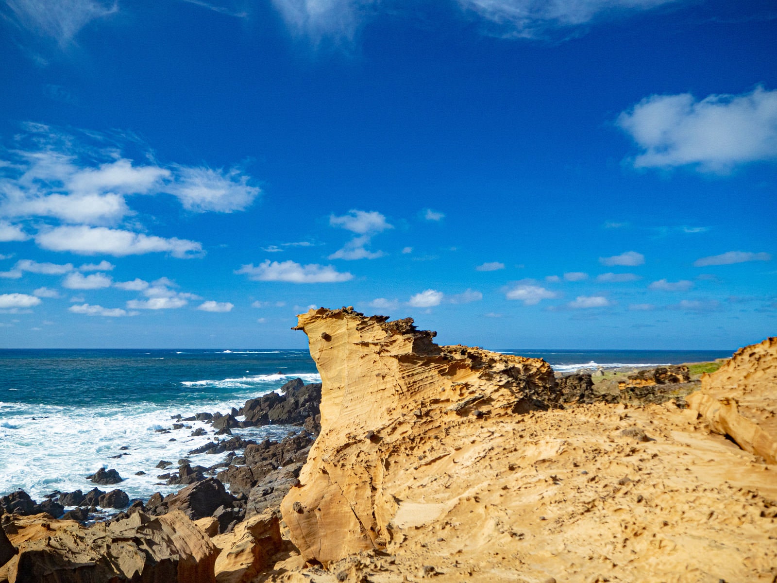 青空と青い海をバックに立つ茶色い岩肌の釜岩の奇岩