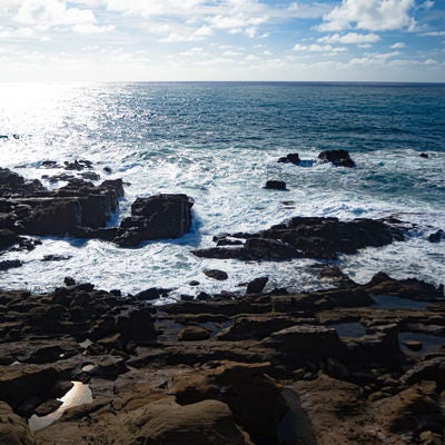 釜岩に打ち寄せる波と光り輝く海原の写真