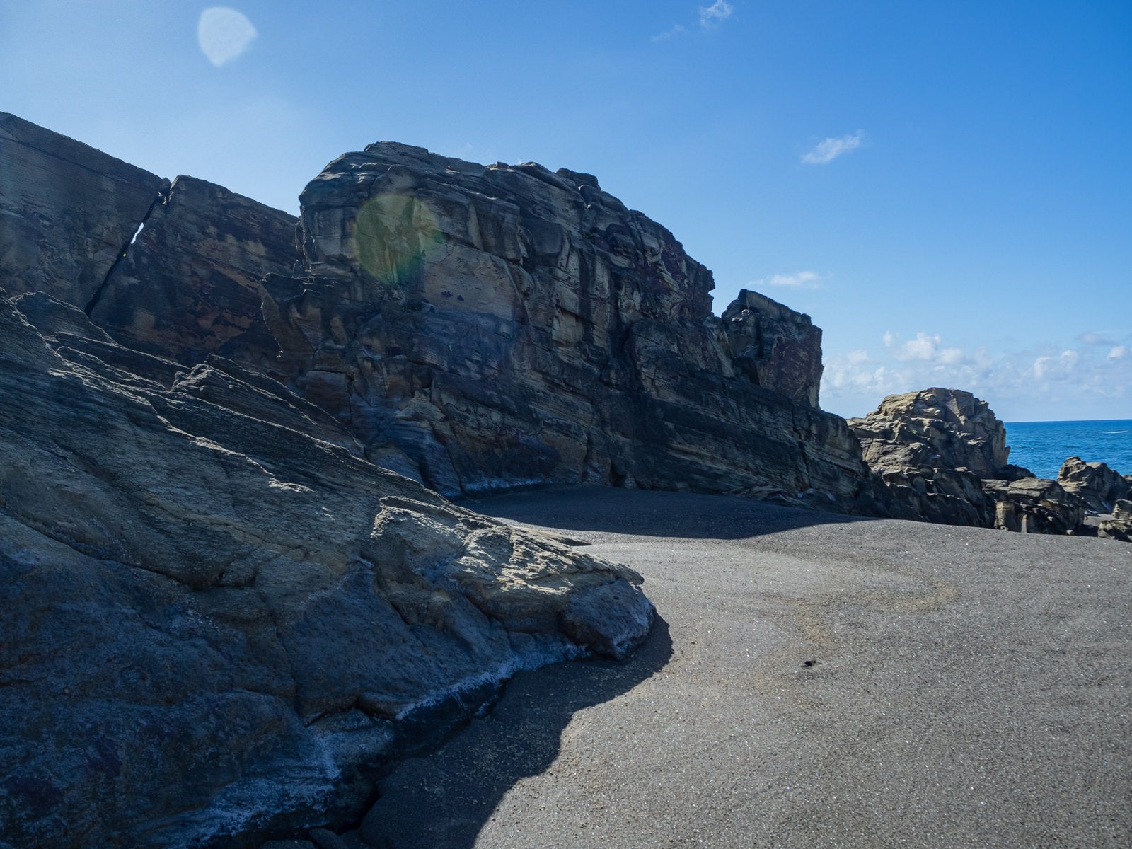 「北の鼻の海岸の黒い砂浜と逆光の中そそり立つ岸壁」の写真