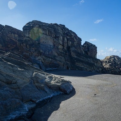 北の鼻の海岸の黒い砂浜と逆光の中そそり立つ岸壁の写真