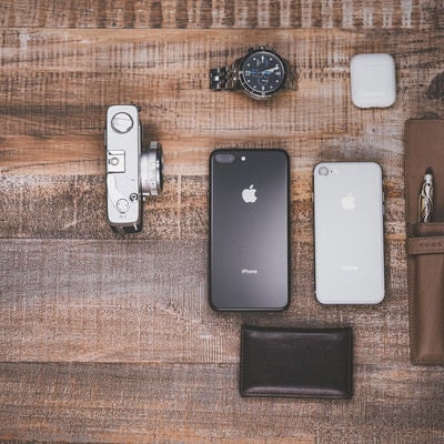 木目のテーブルに並べたiPhoneや腕時計などのガジェット小物の写真