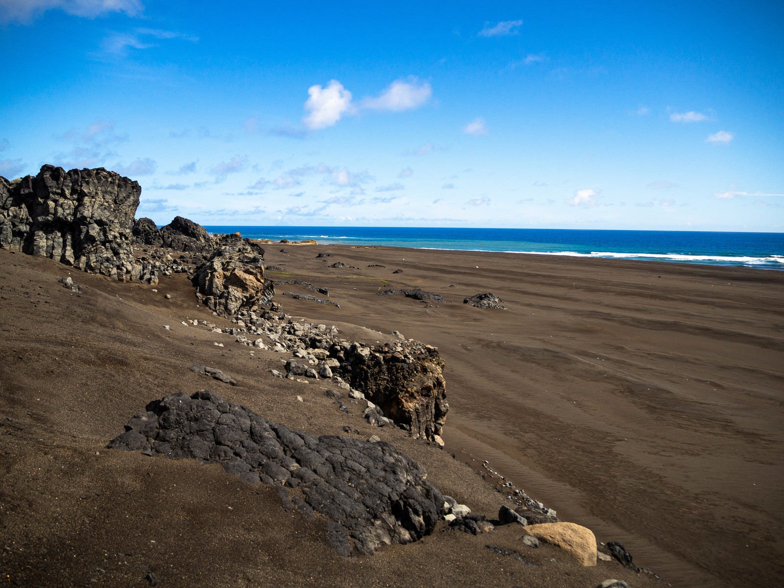 「硫黄島の東海岸のゴツゴツした岩と黒い砂浜」の写真