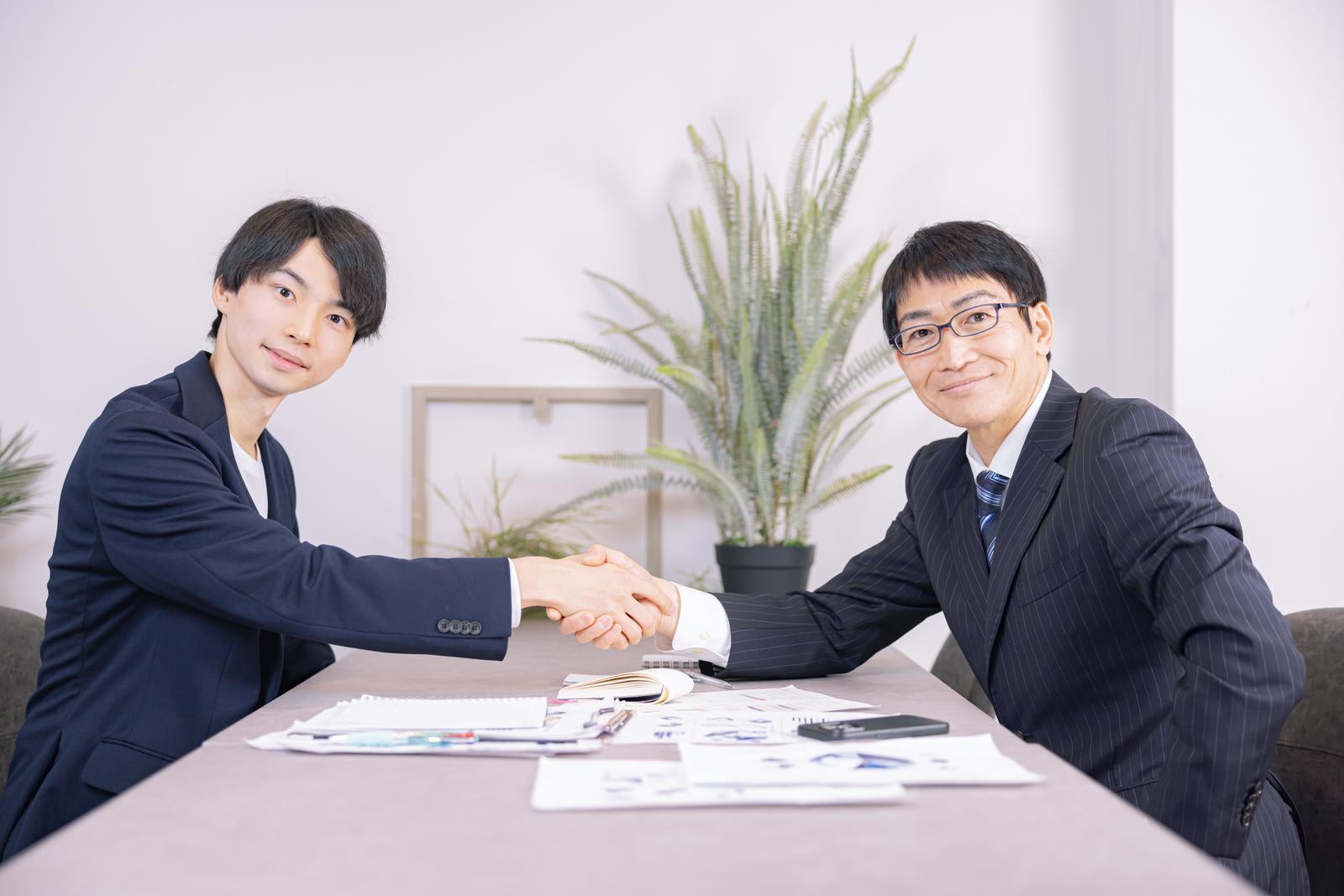 「若い男性と握手を交わす部長」の写真［モデル：たくみ ガーミー］