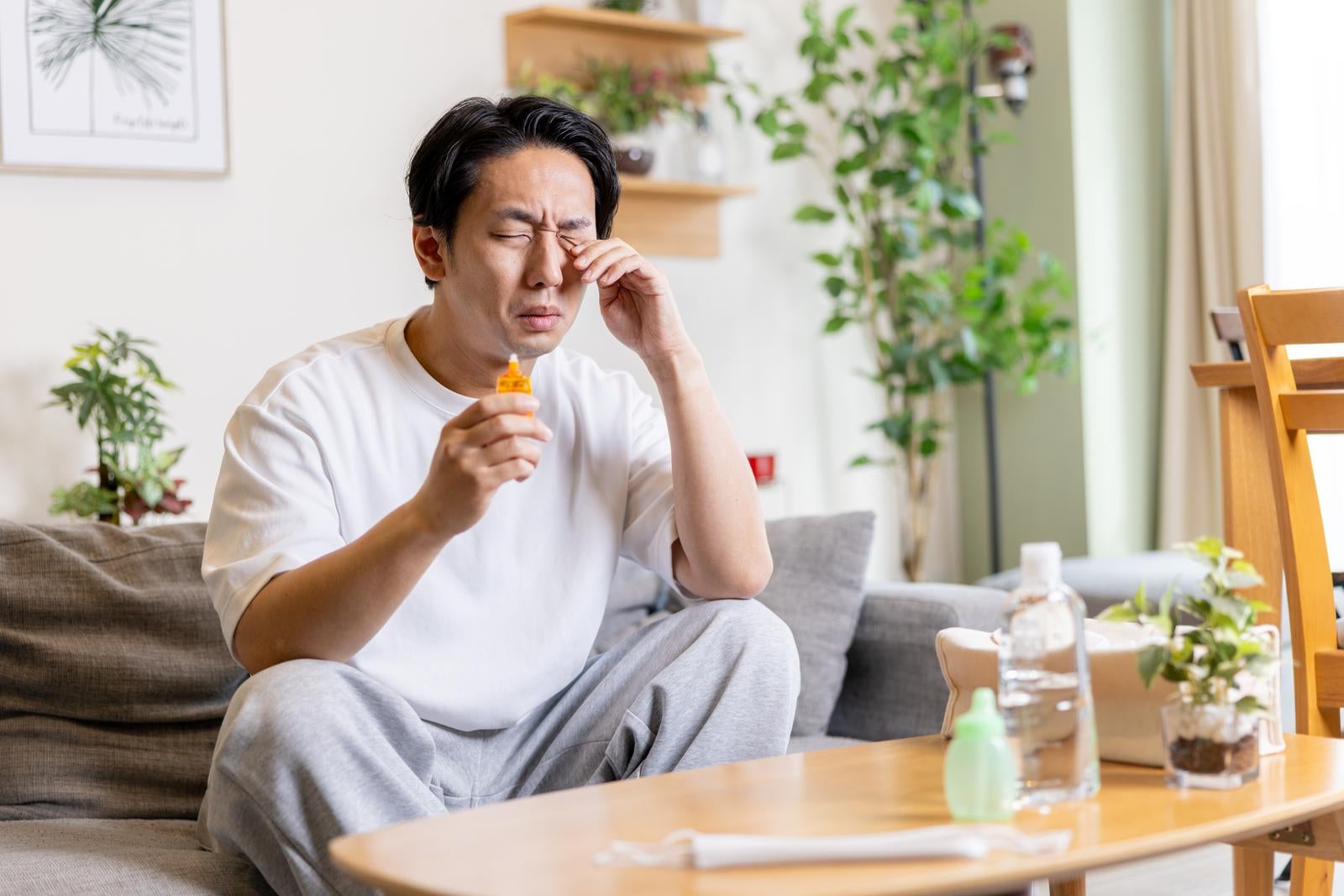 「花粉症で目のかゆみが止まらない男性と目薬」の写真［モデル：大川竜弥］