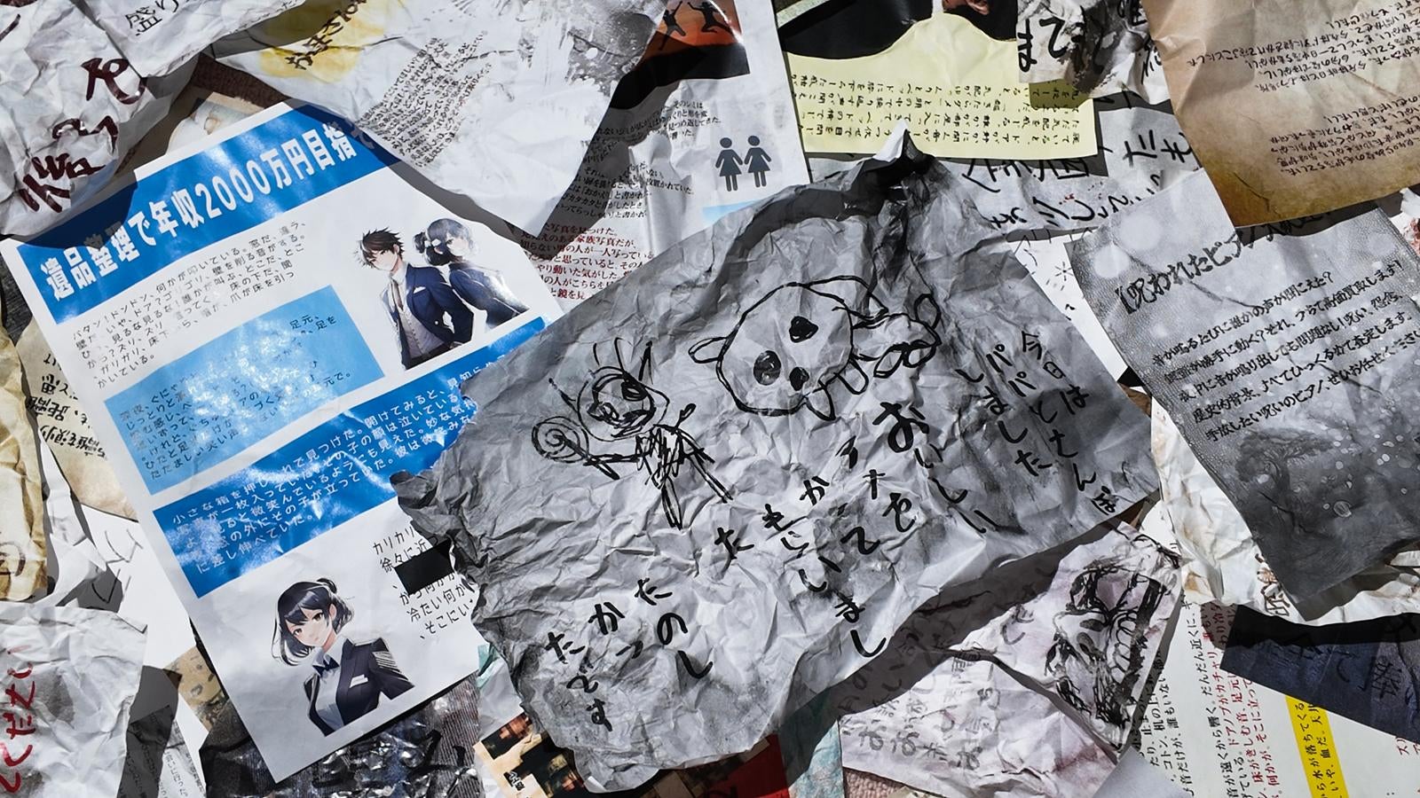 くしゃくしゃになった怪文書やチラシ、子供の落書きが散乱している様子