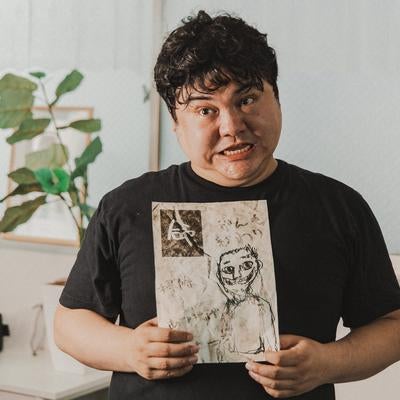 不可解な絵を持ち強張った顔でこちらを見る人物の写真