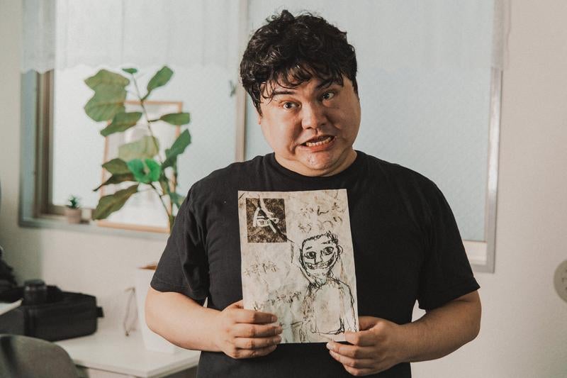 不可解な絵を持ち強張った顔でこちらを見る人物