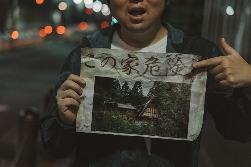 「この家危険」と書かれた怪文書を掲げる男性の写真