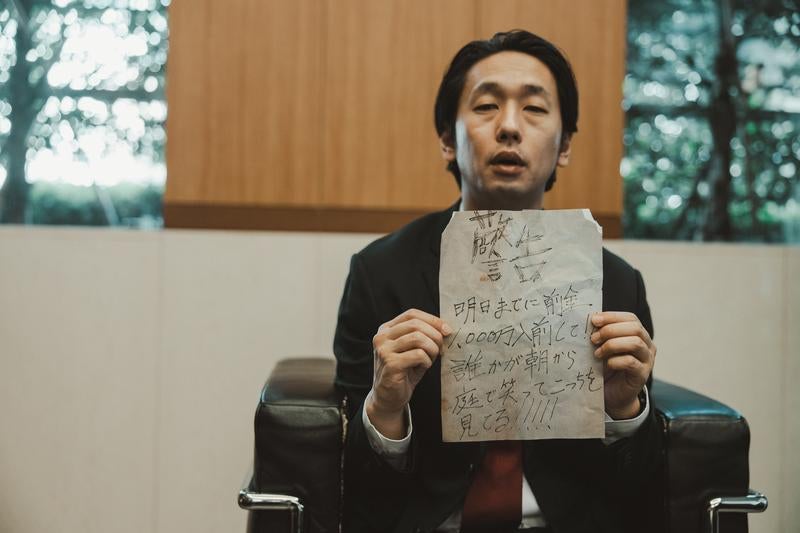 応接室で怪文書を掲げるスーツ男性の写真