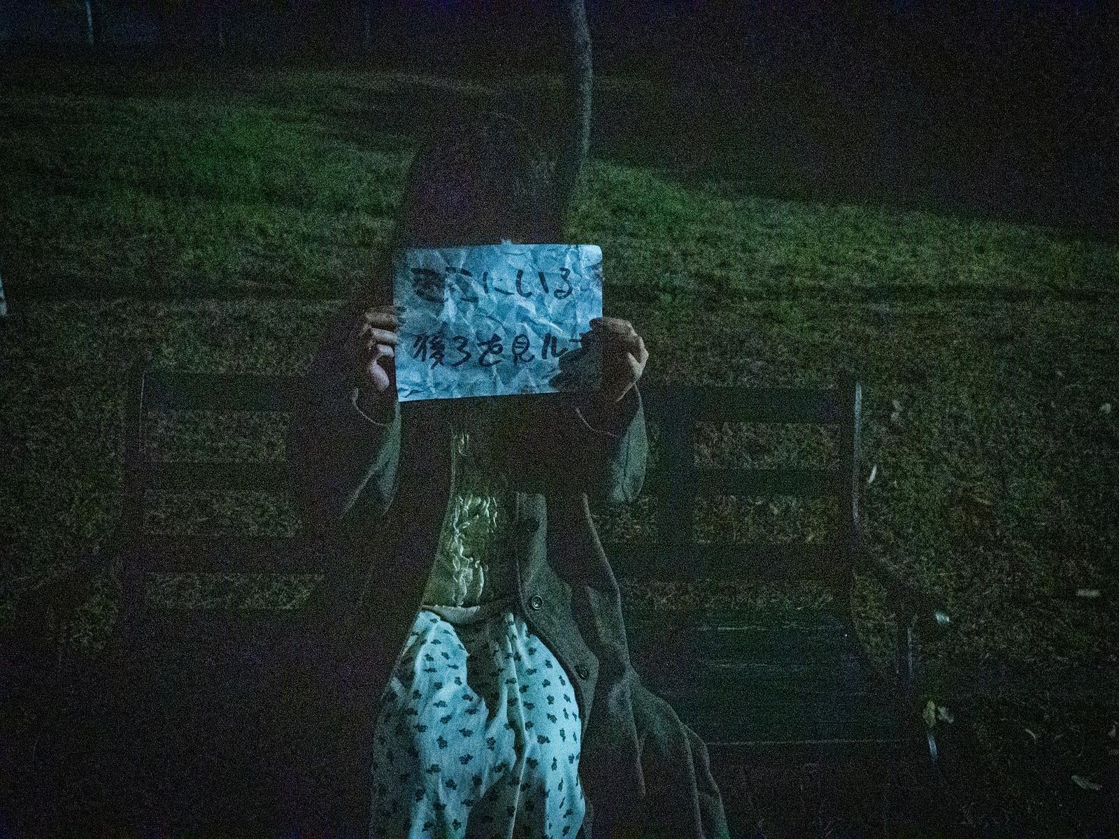 「夜のベンチで怪文書を掲げる謎の女性」の写真［モデル：ラミエル］