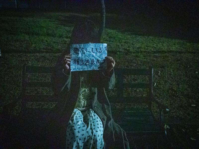 夜のベンチで怪文書を掲げる謎の女性の写真