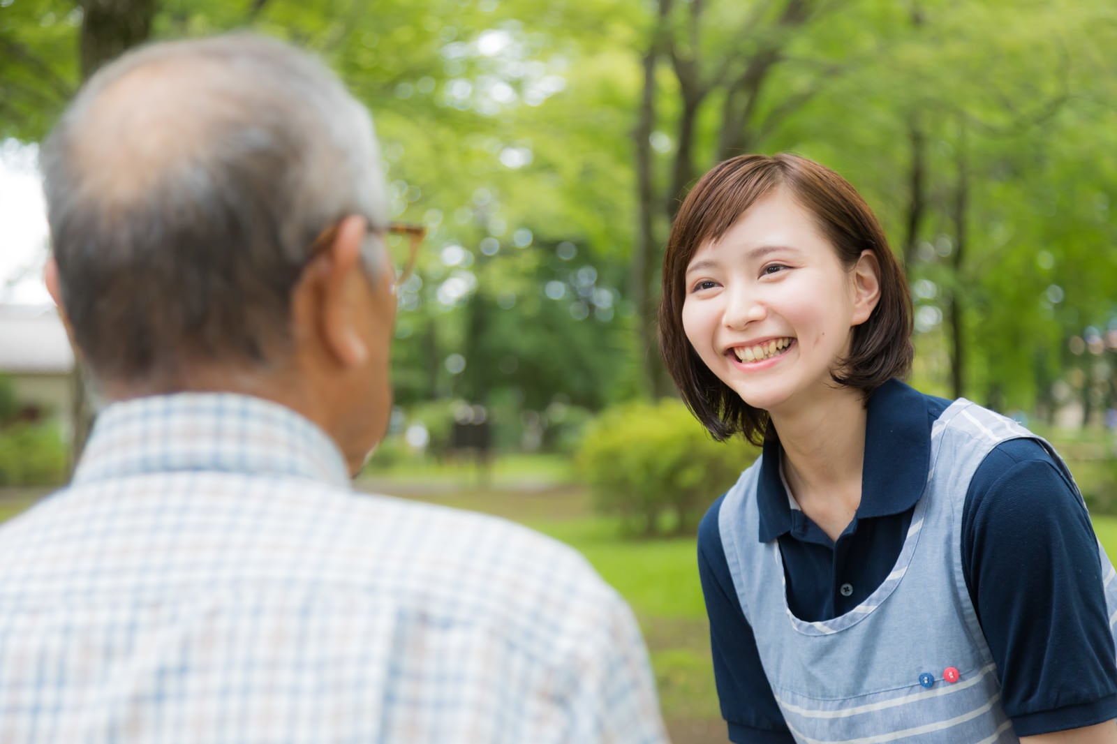 「お爺さんの昔話を笑顔で聞く介護士の女性」の写真［モデル：まーちゃん yumiko］
