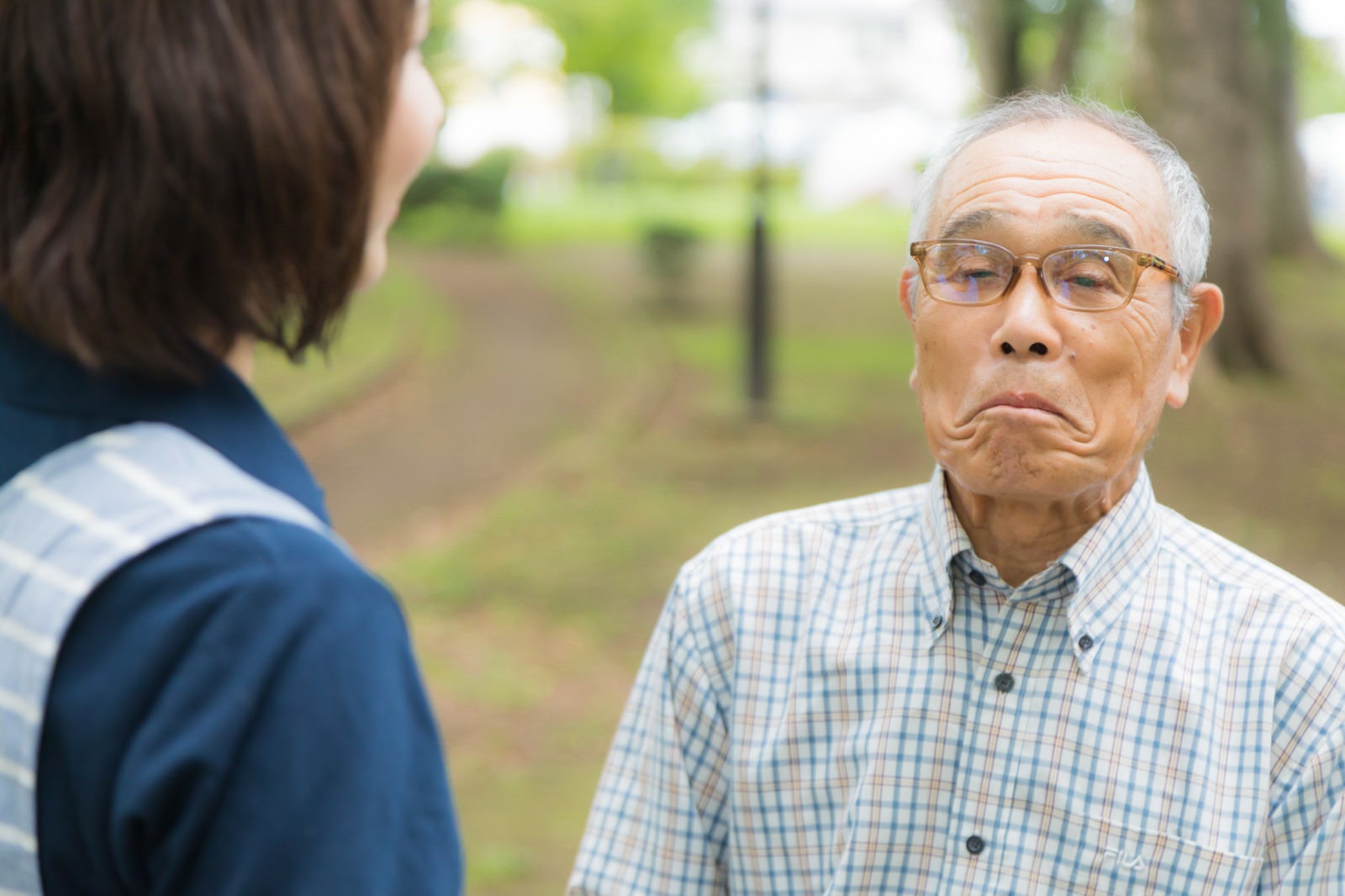 「口をへの字にして動かない高齢者と説得するヘルパー」の写真［モデル：まーちゃん yumiko］