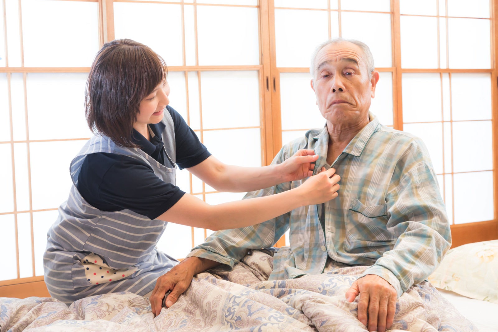 「高齢者のパジャマのボタンをつける出張介護士」の写真［モデル：まーちゃん yumiko］