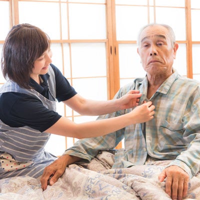 高齢者のパジャマのボタンをつける出張介護士の写真