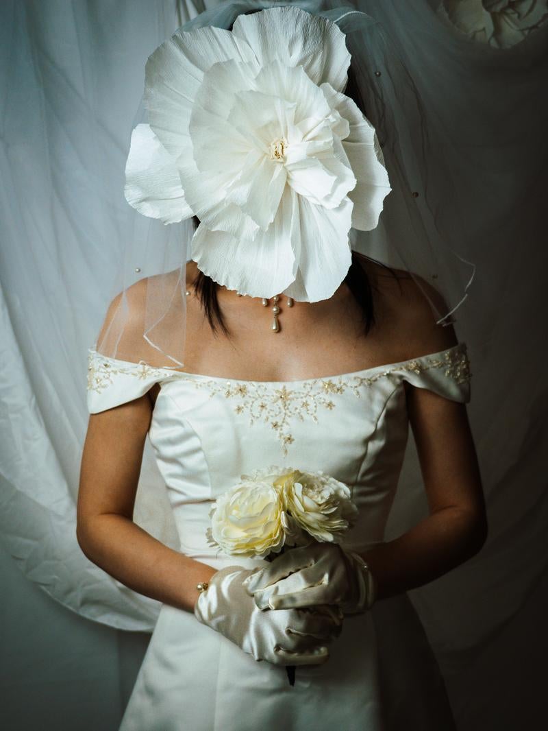 白い大きな造花で顔を隠した白いドレスの花嫁がブーケを持っている写真