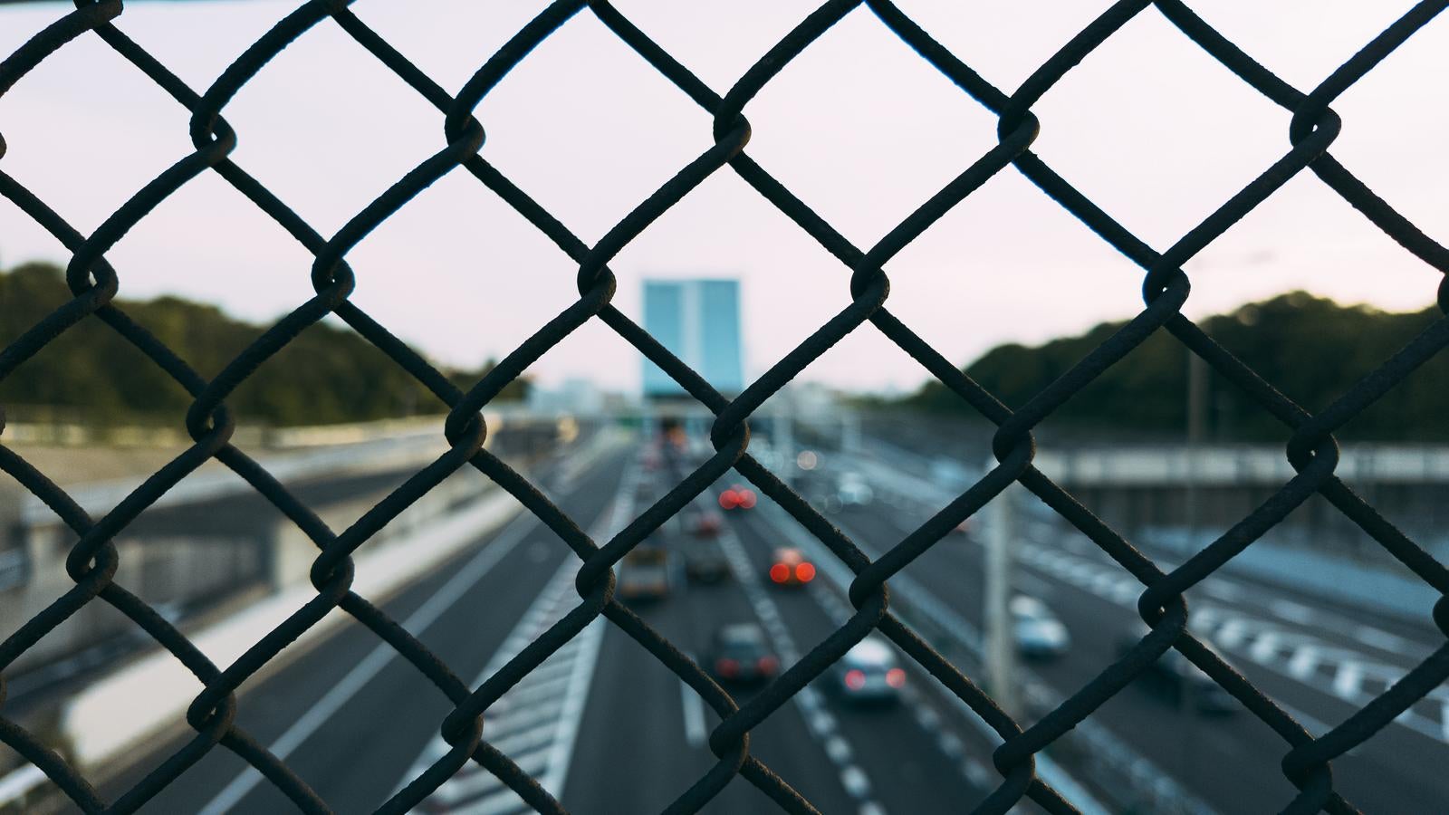 「フェンス越しに見る都市と高速道路を走行する車」の写真