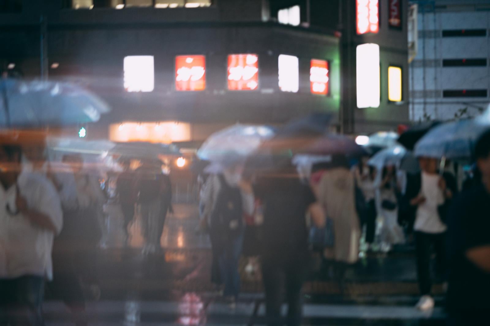 「錦糸町駅前の横断歩道を渡る傘をさす通行人」の写真