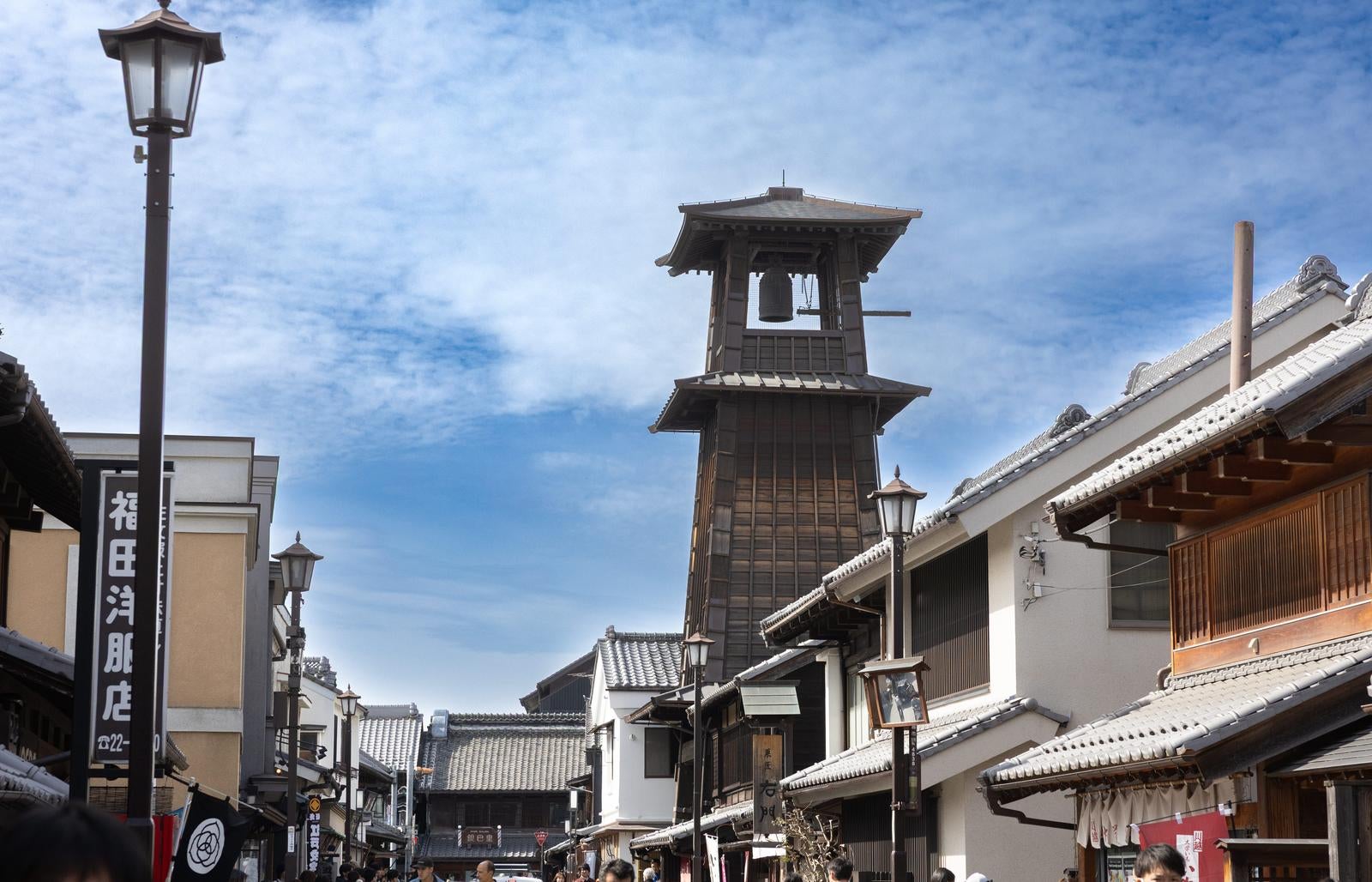 川越の時の鐘を中心に白壁と黒木造の建物が並ぶ古い町並みと観光客