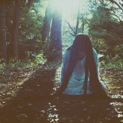 森の中で蹲りながら近づいてくる女性の写真