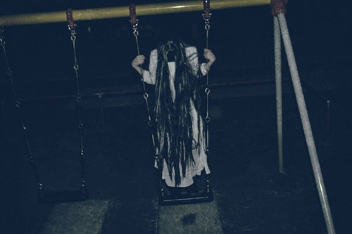 夜の公園で立ちこぎに夢中な髪の長い女性の写真