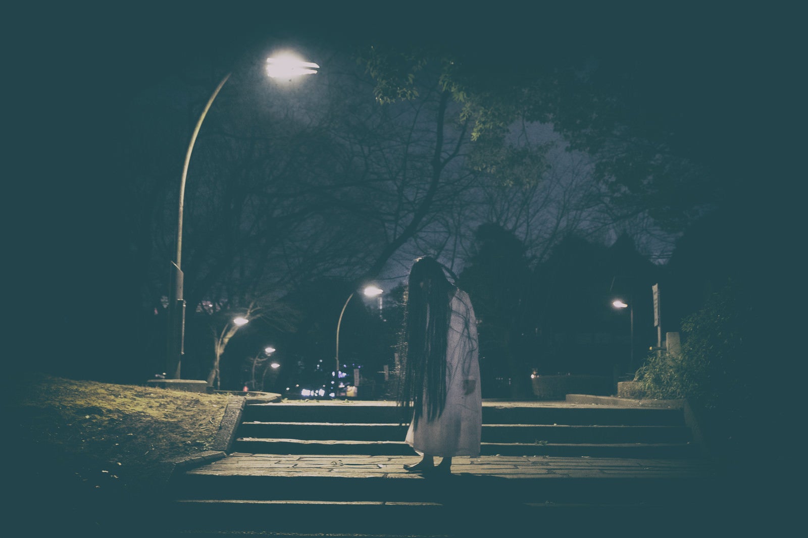 「公園のライトの下で佇む髪の長い女性」の写真