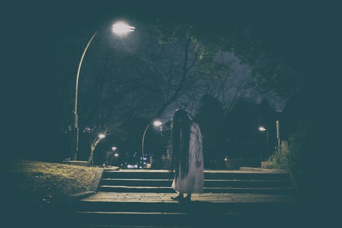 公園のライトの下で佇む髪の長い女性の写真
