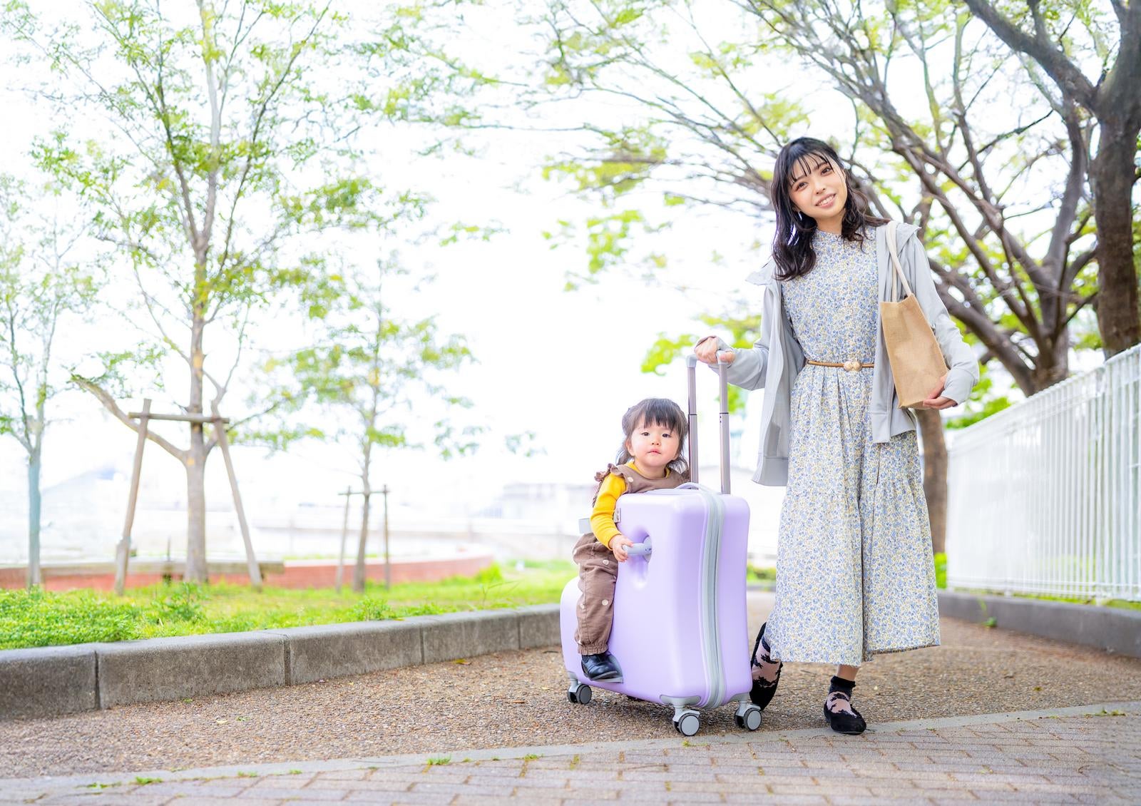 「キャリーケースに座る子どもとおでかけするママのお散歩風景」の写真［モデル：高尾実生］