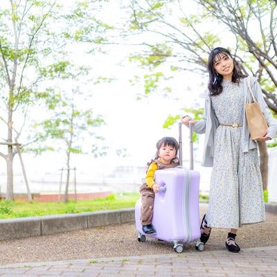 キャリーケースに座る子どもとおでかけするママのお散歩風景の写真