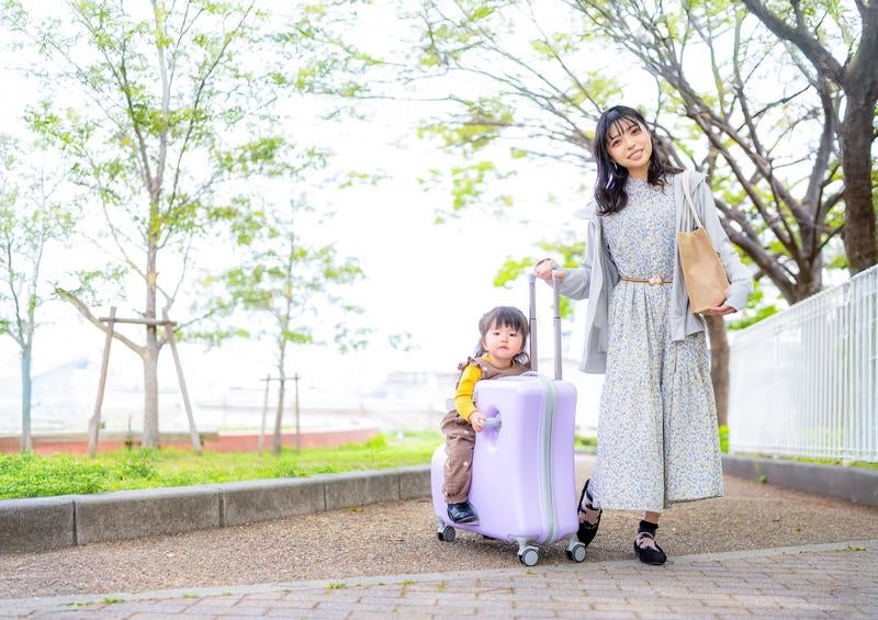 キャリーケースに座る子どもとおでかけするママのお散歩風景の写真