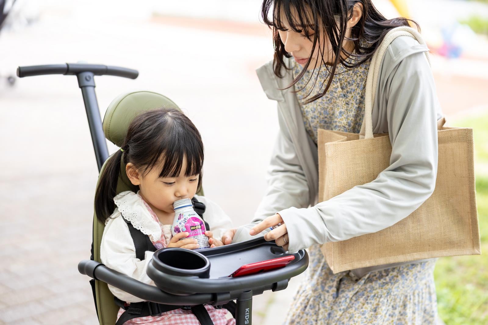「ベビーカー上でスマホを見ながらドリンクを飲む子ども」の写真［モデル：高尾実生］