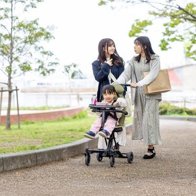 新緑の公園道でベビーカーを押す女性と子どもの写真