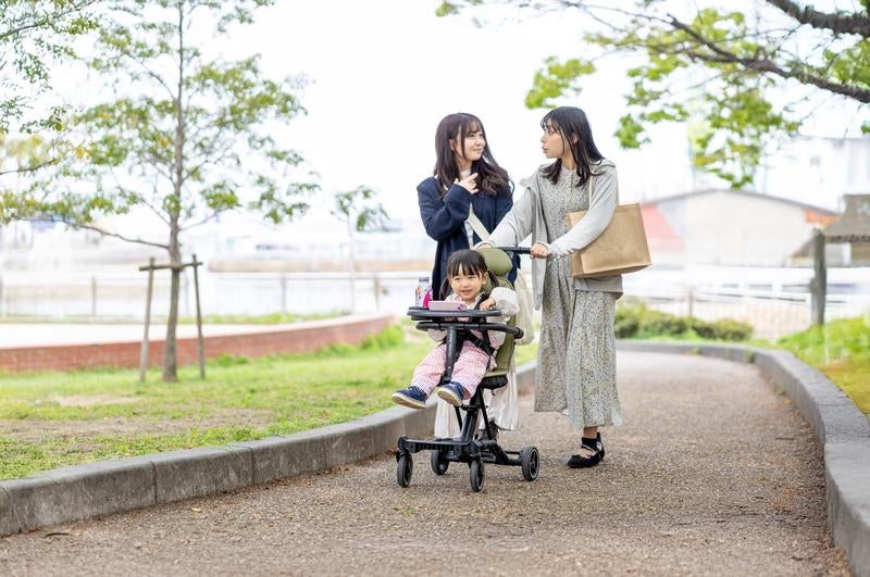 新緑の公園道でベビーカーを押す女性と子どもの写真