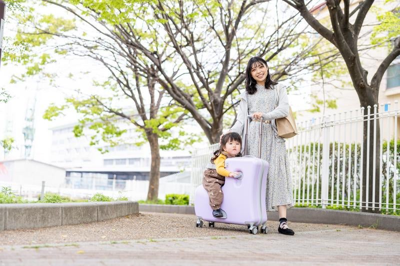 キャリーケースの上で微笑む子どもとお母さんの写真
