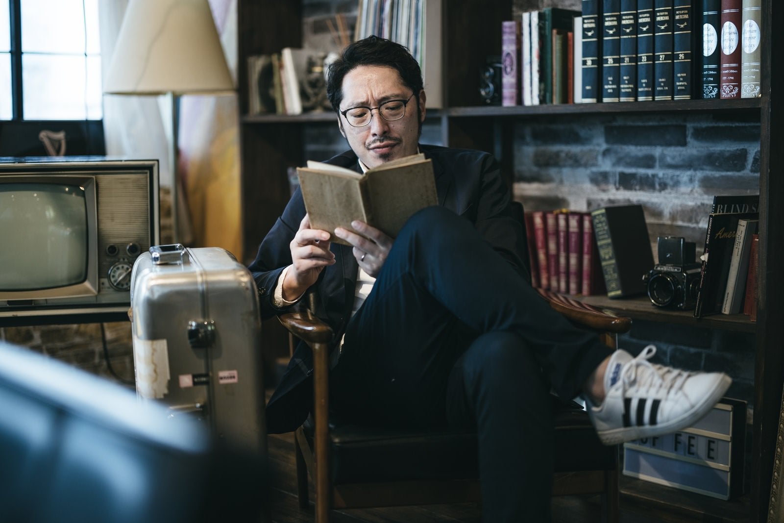 「スーツケースと読書を楽しむ男性」の写真［モデル：ゆうせい］