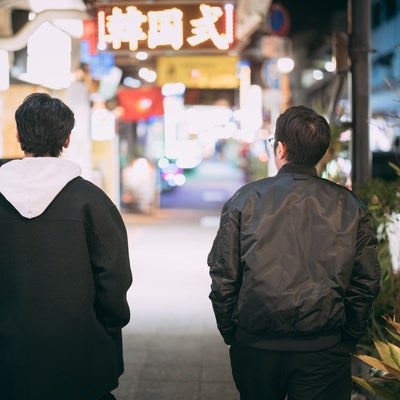 ネオンが輝く繁華街を歩く男性ふたりの写真