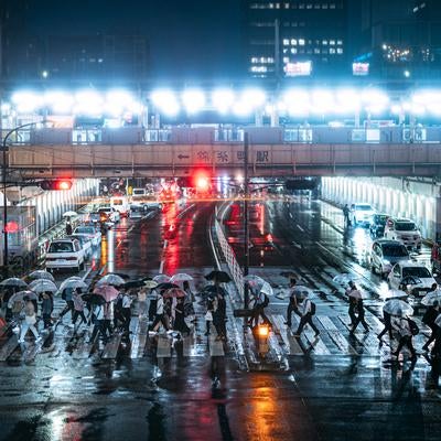 夜の錦糸町駅前の横断歩道を傘を差して横断する人々の写真