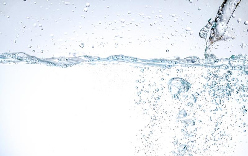 透明な水面に落ちる水滴と立ち上がる気泡の写真