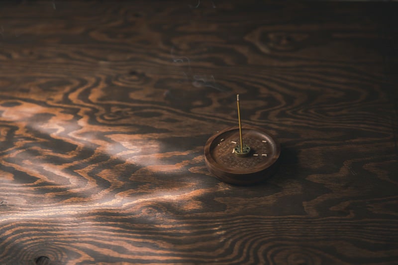 木目の机に置かれたお香立てから立ち上る煙の写真