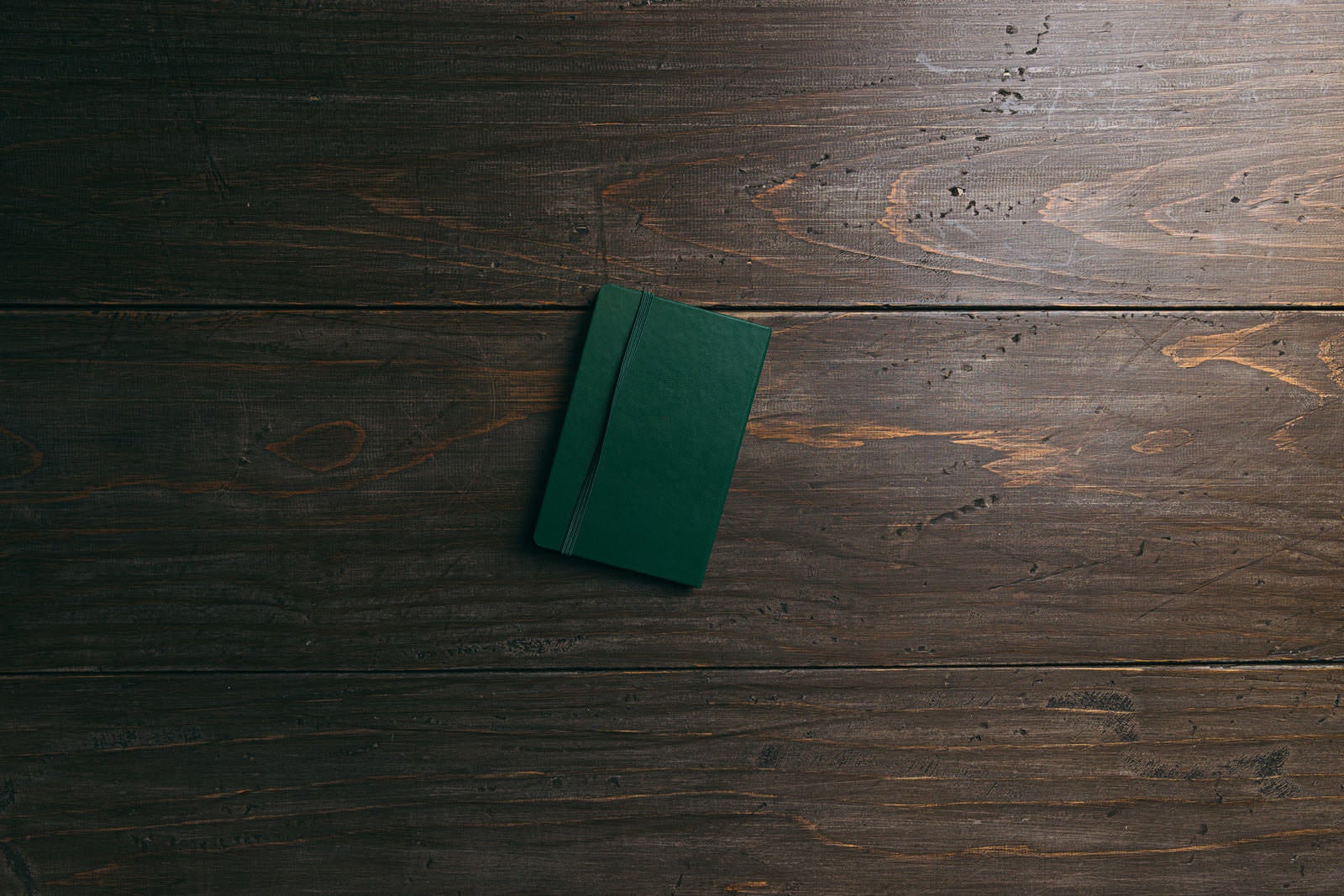 濃い茶色の木目テーブルの上にゴムバンド付きの緑色の手帳が1冊置かれている俯瞰写真