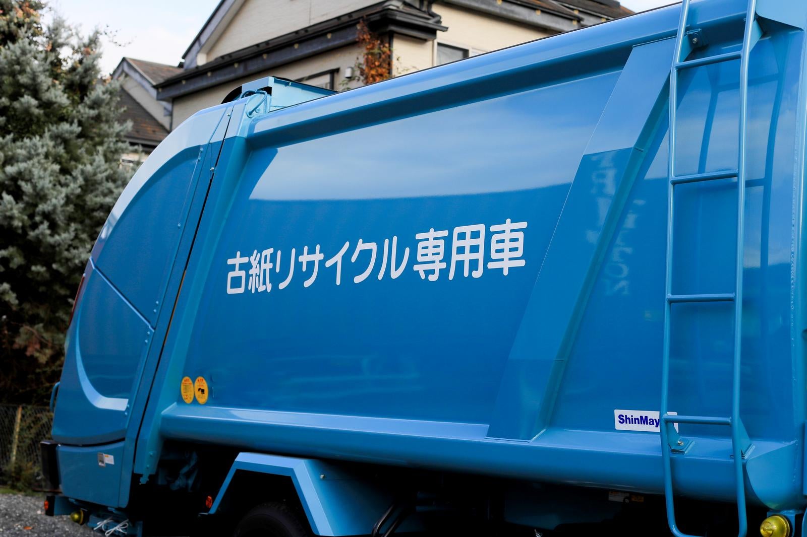 古紙リサイクル専用と書かれた青いボディの回収トラックが住宅地に停まっている