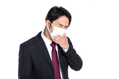 マスク着用しながら咳が止まらない会社員の写真