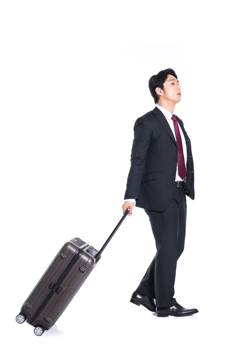 「スーツケースを引きずるビジネスマン」の写真［モデル：大川竜弥］