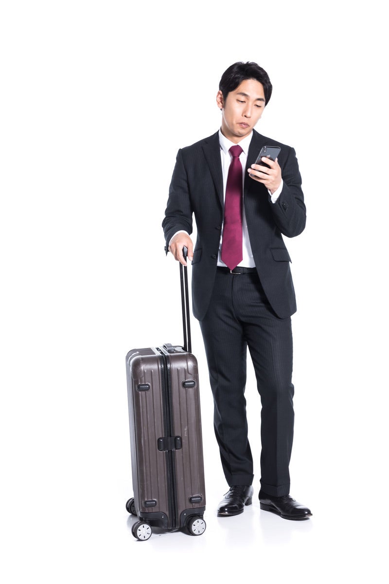 「スーツケースを持ってチェックイン時間を確認する会社員」の写真［モデル：大川竜弥］