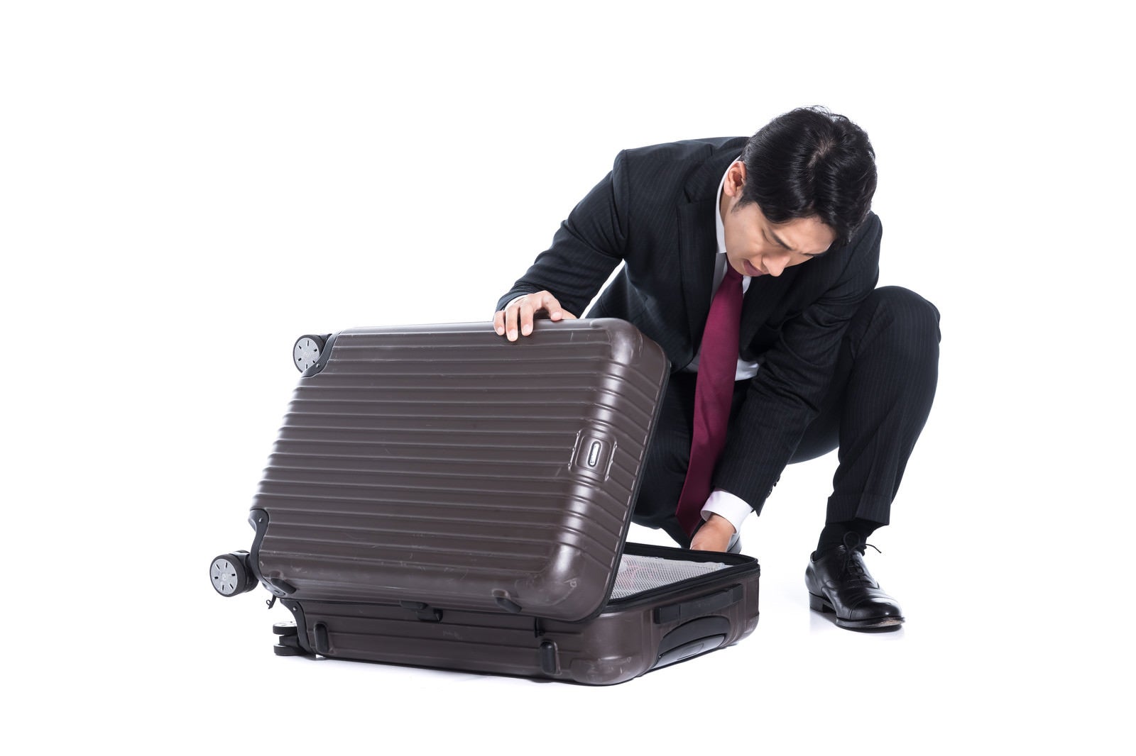 「スーツケースに荷物を詰め込むビジネスマン」の写真［モデル：大川竜弥］