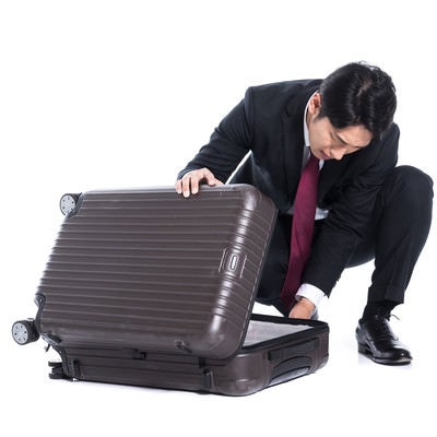 スーツケースに荷物を詰め込むビジネスマンの写真